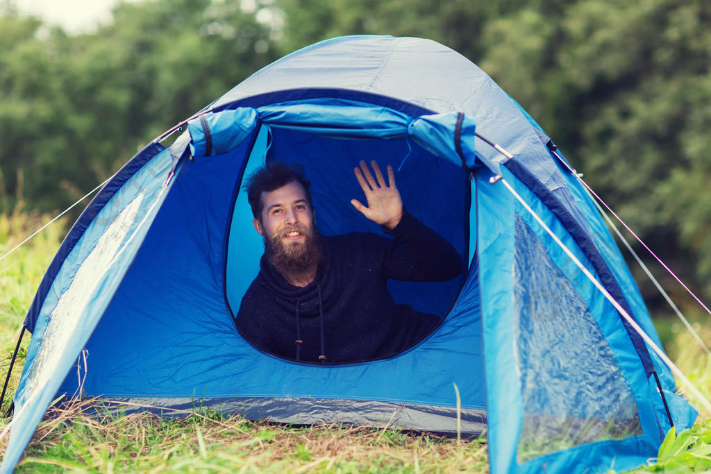 露营,旅行,旅游,远足和人们观念-微笑男游客留着胡子挥舞着的手在帐篷